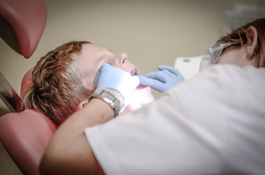 dentist-woman-wearing-white-gloves-and-white-scrubsuit-checking-boy-s-teeth-52527 A young boy receiving a dental examination by a professional dentist in a clinic setting.