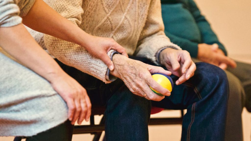 person-holding-a-stress-ball-339620 An elderly person receives support from a caregiver, holding hands indoors, showcasing compassion.