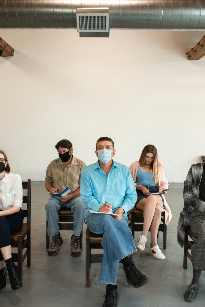 pexels-photo-5756561-5756561 A diverse group of adults seated indoors, engaged in learning activities, all wearing masks.